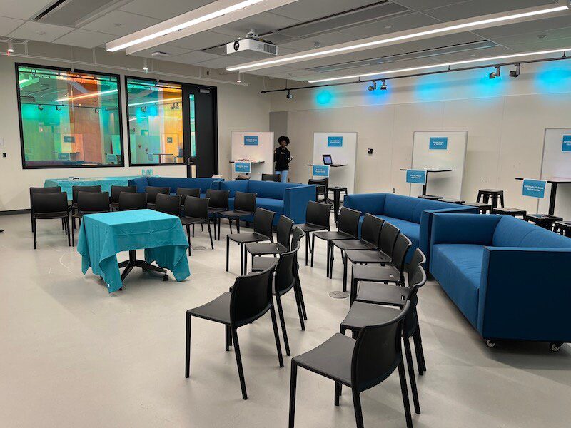 Several standing table stations, couches, and chairs are set up in rows in the Design Loft room.